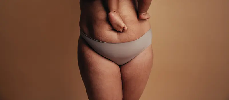 Cropped shot of a healthy female carrying her baby. Close-up of a woman in underwear with feet of child on postpartum belly.