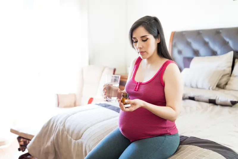 Good looking woman taking medicines for pregnancy while sitting on bed
