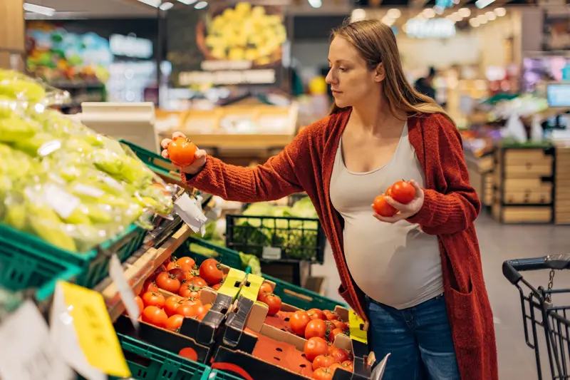 A pregnant woman makes a healthy choice as she selects organic vegetables and fruits at the vibrant organic market, prioritizing her well-being and her baby's health