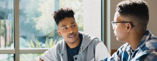 Sitting at the same table, the two male teenage friends talk during class.