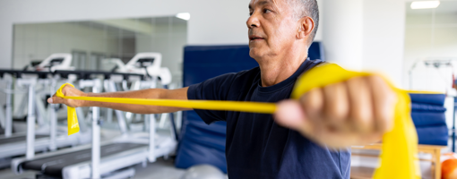 Mature Latin American man doing physical therapy exercises using a stretch band at a rehabilitation center