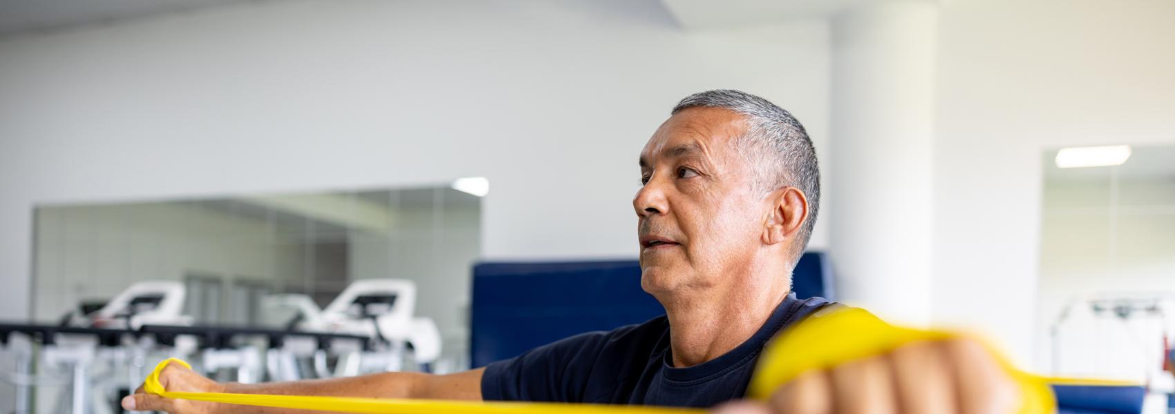 Mature Latin American man doing physical therapy exercises using a stretch band at a rehabilitation center