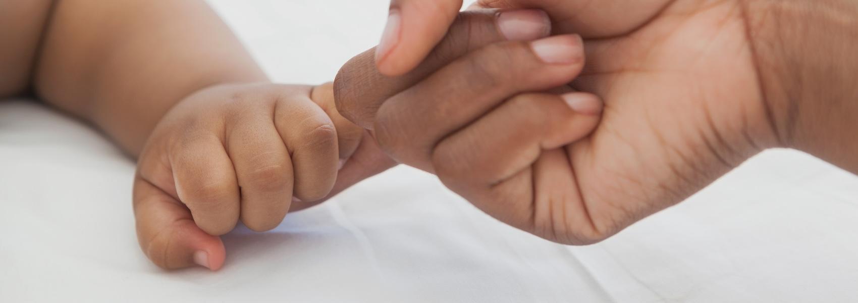 Extreme close-up of a baby holding mother's finger on white surface