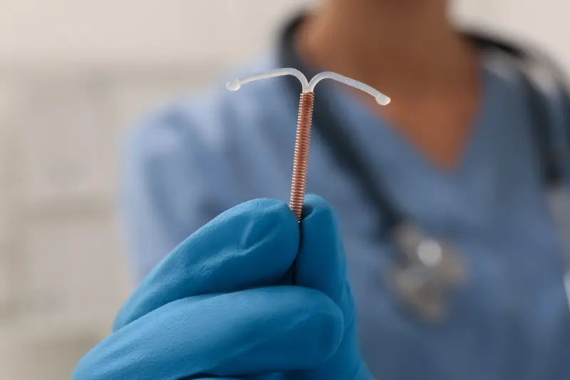 Doctor holding T-shaped intrauterine birth control device on blurred background, closeup