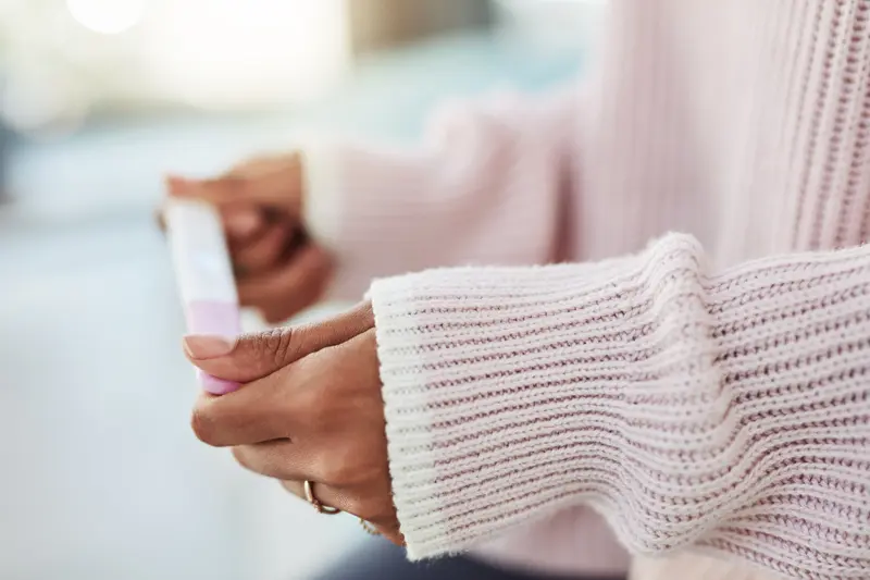 Close-cropped shot of a person's arms (wearing a pink sweater) and hands, holding a pregnancy test