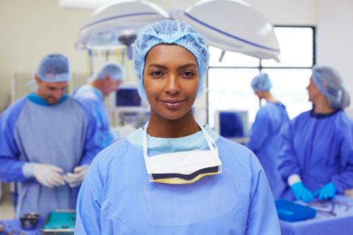 Portrait of an attractive ethnic nurse standing in a busy operating room