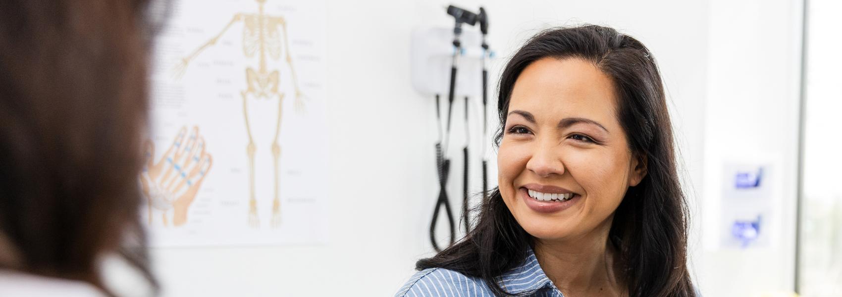 The mid adult female patient sits on the examination table and smiles while listening to encouraging news from the doctor.