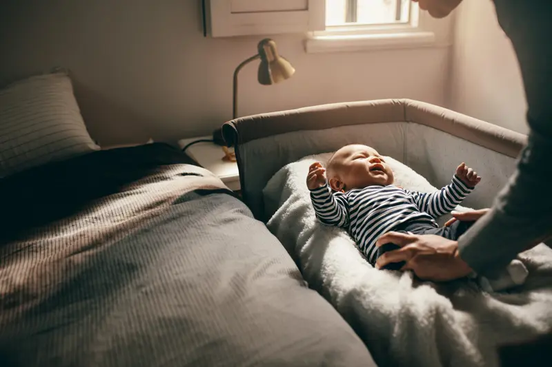 Woman attending to her crying baby trying to pacify him. Mother putting her baby to sleep in his bassinet.