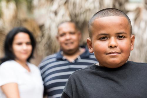 Hispanic child posing smiling with his parents in the background