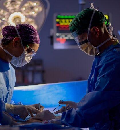 Two surgeons, facing each other, operate on a patient in a dramatically lit OR