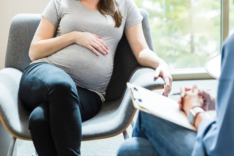 The unrecognizable expectant mother lays her hand on her baby bump as she shares her feelings with the unrecognizable therapist.