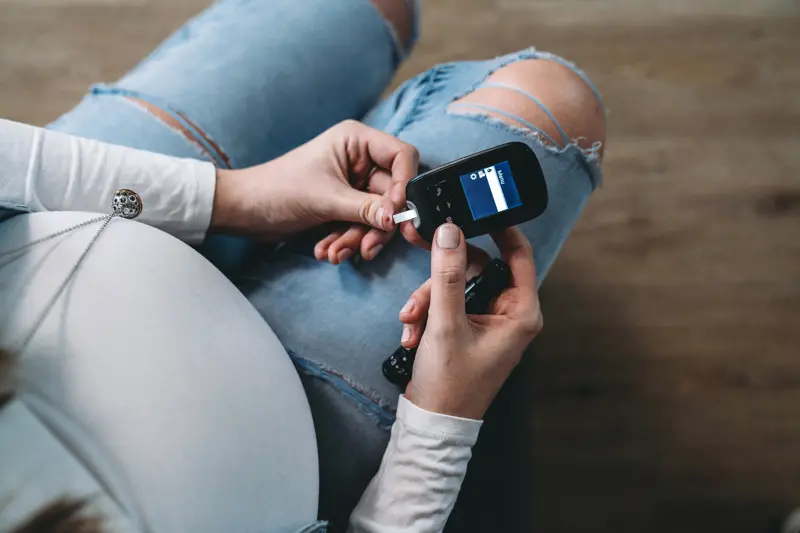 Pregnant woman testing blood sugar at home. She's puncturing her finger.