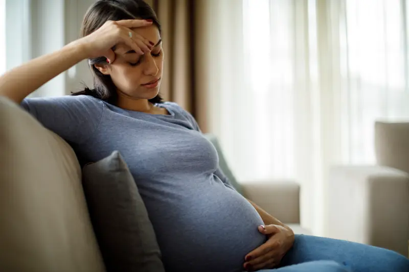 Tired stressed pregnant woman sitting on a couch and holding her belly